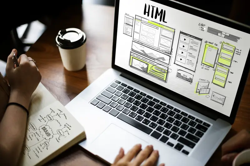 Person working on a laptop with website wireframes and HTML layout displayed on the screen, representing custom web design and development.